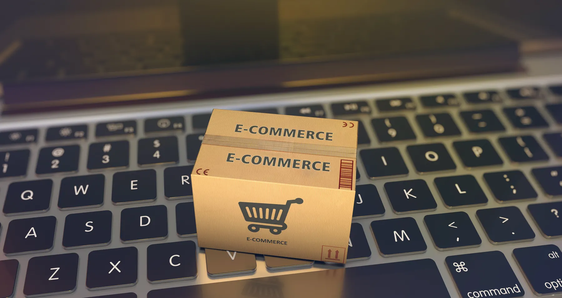 Parcel marked with a shopping cart and the word e-commerce resting on a laptop keyboard